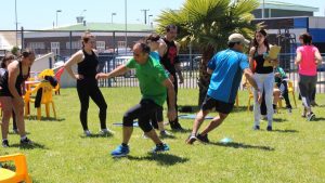 A group of adults exercising on a sunny grass field near a palm tree